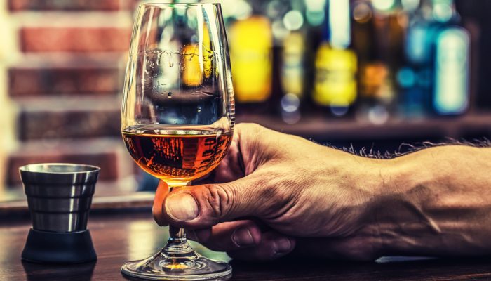 male-hand-holding-glass-of-brown-liquor