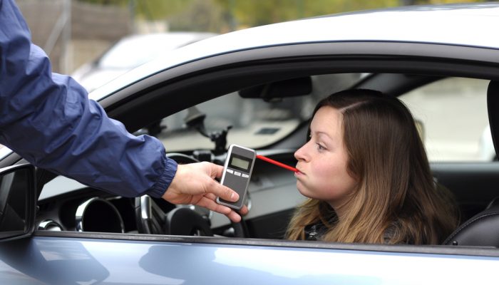 young female driver being subject to test for alcohol content with use of breathalyzer