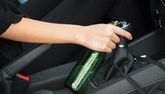 closeup inside vehicle of hand holding onto green beer bottle and stick shift