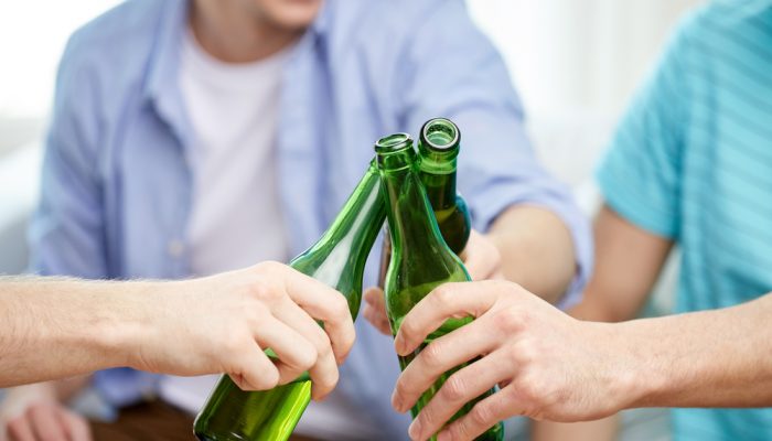 close up of male friends drinking and clinking beer bottles at home